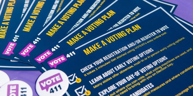 VOTE411 Make a Voting Plan informational brochures and buttons arranged on a purple table.