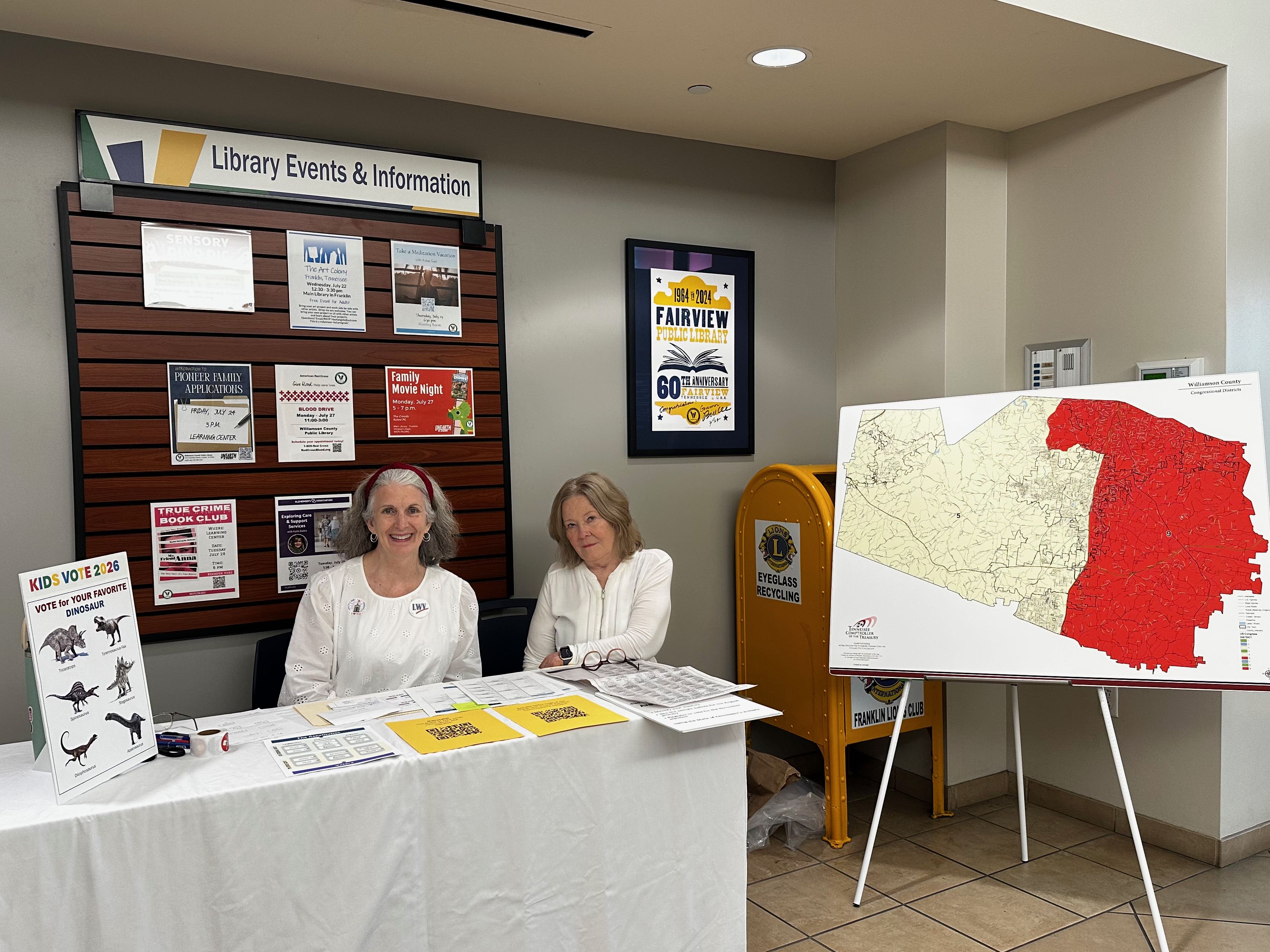 Two women sitting behind a table with election information displayed